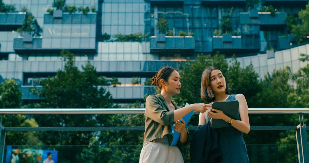 Two young Asian businesswomen meeting business strategy discussion talk outside modern office building. Sustainable business outdoor. Hexagon's Digital Twin Industry Report has found that companies using digital twins report an average cost saving of 19% and a 15% reduction in emissions
