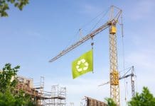 Why ESG is not enough: The critical role of carbon and cost estimating in sustainable construction A construction site with a crane hoisting a green flag with a recycling symbol.