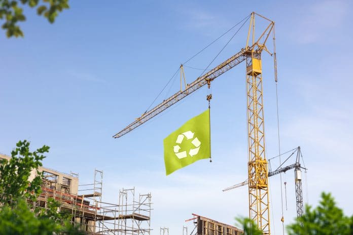 Sustainable Building A construction site with a crane hoisting a green flag with a recycling symbol.