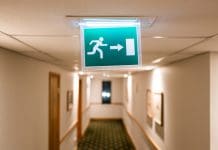 Who is the Fire Safety Building Regulation Group and what do exactly do they do? Shallow focus of a generic Fire Escape sign seen hanging from the ceiling of a hotel lobby in the UK. Seen during late at night, many of the guests are in there rooms, representing the FSBRG