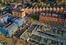 NHBC’s Building for Tomorrow becomes BEYOND ’25 LIVE Aerial view of a residential construction site. Brick townhouses are complete, while adjacent buildings are under construction, surrounded by scaffolding and building materials. The scene shows a mix of finished and unfinished structures, representing topics to be discussed at BEYOND '25 LIVE.