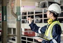 Building maintenance backlog: How retrospective digitisation can transform the crisis Building inspector man using digital tablet pointing at plumbing pipeline system. Asian male worker in green vest, protective ear muffs and safety helmet working for building maintenance inspection representing Building maintenance backlog and retrospective digitisation