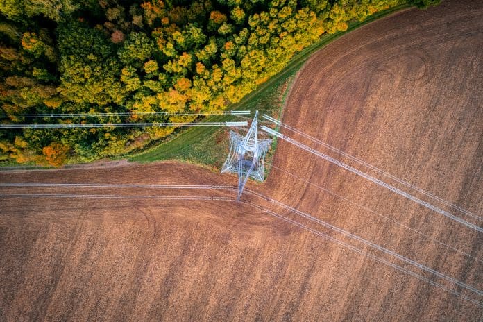 Electricity line changing direction 400kV extra high voltage electricity line changing direction above cultivated field contracting with autumn forest, shot from above with drone, representing the new planning and infrastructure bill