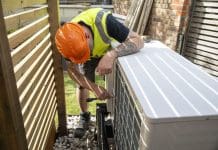 The Heat Pump Summit returns to the University of Oxford A male electrician installing a heat pump in a garden on a sunny day.