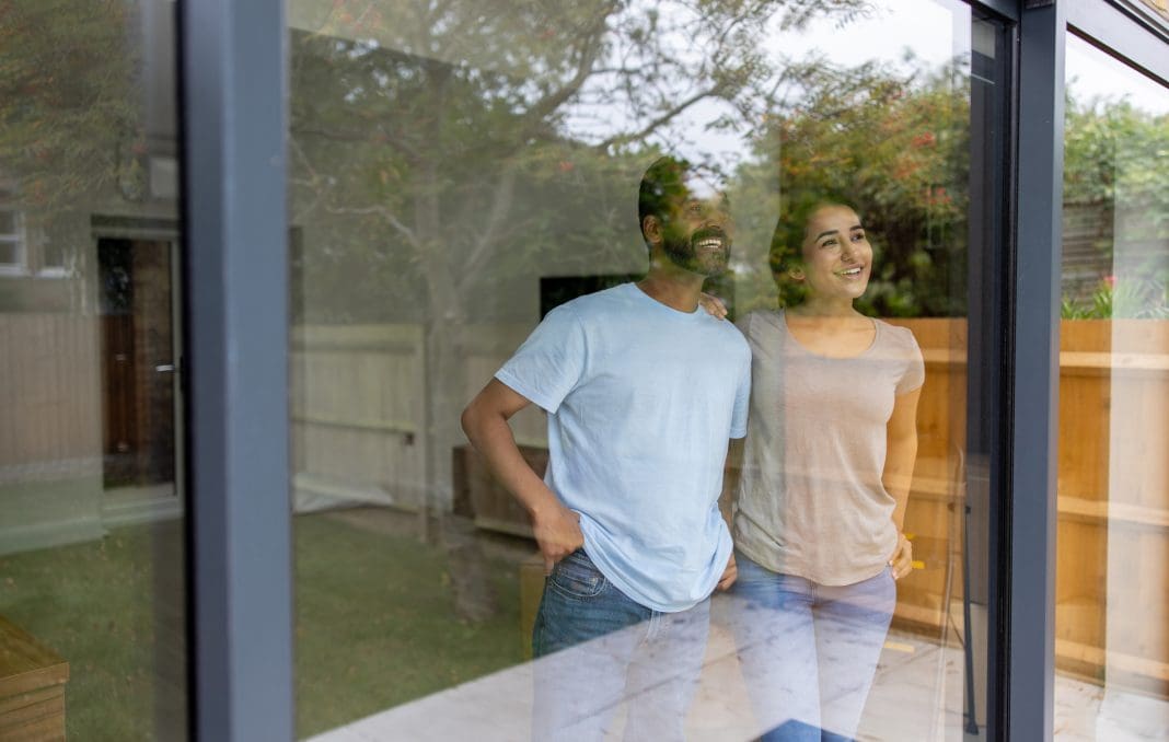Happy Indian couple in a house looking through the window and smiling - moving house concepts, representing construction industry customer satisfaction