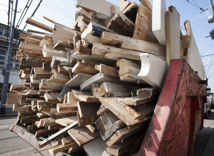 Rust red skip loaded with a pile of old wood from home for recycling