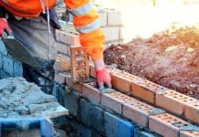 Digital data and technology: Helping housebuilders meet expected outputs Industrial bricklayer laying bricks on cement mix on construction site. Fighting housing crisis by building more affordable houses concept, representing digital technologies