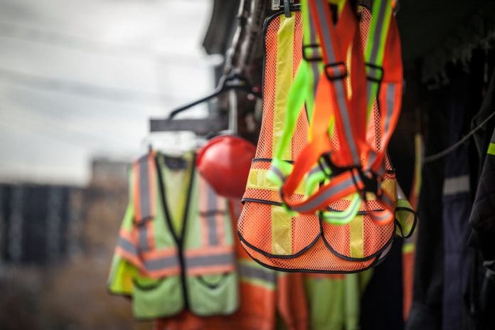 Picture of PPE, or personal protective devices, for sale in a shop, haning. Yellow and Orange vests, harnesses and helmets are visible, representing building control webinar