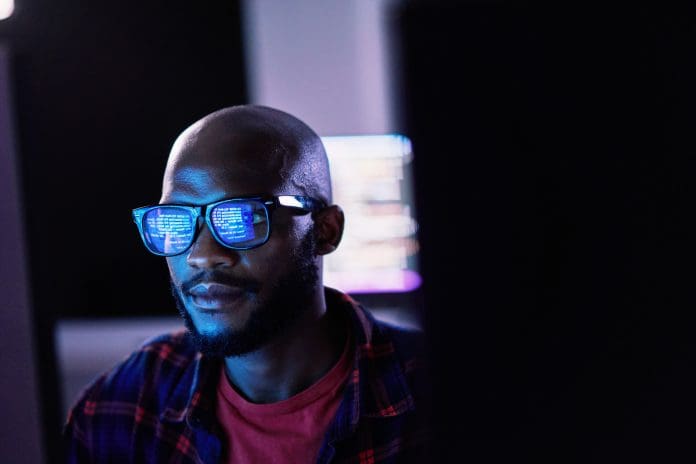 Cyber security, black man and code reflection in eyewear, hacking and software update in office. African American male employee, programmer or IT specialist with glasses, focus and cloud computing, representing digital technology