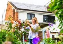 RIBA and The King’s Foundation team up to launch champion retrofit A mid adult woman in her 30s taking care of the flowers in his garden, by performing tasks such as pruning. She is dressed casually in a light blue shirt and blue denim jeans. In the background is her sustainable semi-detached home, with solar panels on the rooftop, representing the new RIBA and king's foundation retrofit scheme