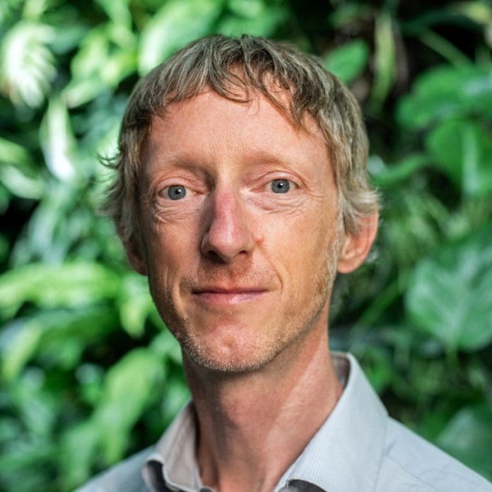 A headshot of Stephen Hill of Arup standing in front of a green background looking towards the camera