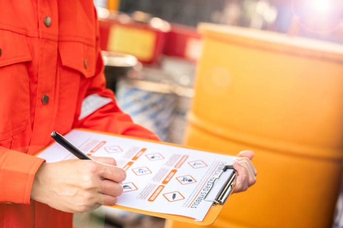 An environmental engineer is using hazardous material checklist form to correct the chemical safety at the factory storage area. Industrial work, photo applied with sunlighting and len flare effect, representing building safety case reports