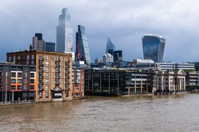Dockside development beside the River Thames, in the financial heart of the City of London. The modern riverside development is made up of residential apartments, hotels, restaurants and office space, making it a popular area in the heart of the financial district. Tall office buildings can be seen in the background, rising above the city landscape, well known recognisable landmarks in the English capital, representing flood risk