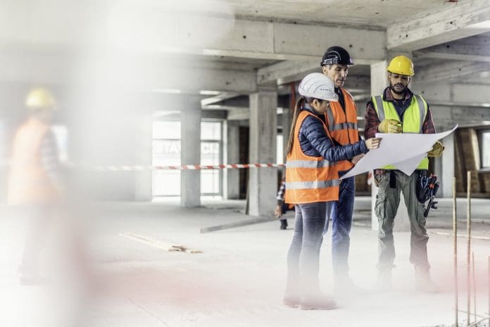 Building contractors consulting architect on plan Two construction workers consulting a female Asian architect about her blueprints, representing: Two construction workers consulting a female Asian architect about her blueprints.