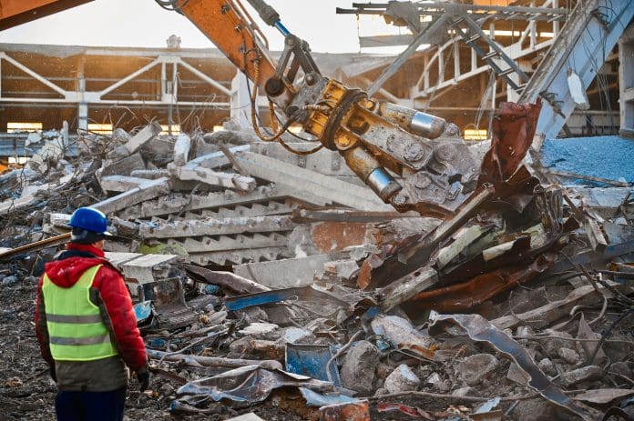 Powerful excavator destroyer removes debris under professional worker control at demolish site under blue sky on winter day, representing a circular economy