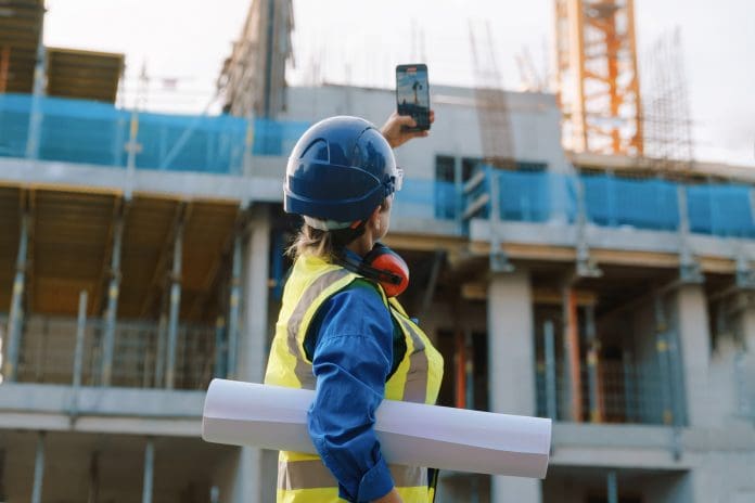 Female construction worker checks plans on site while managing project progress in urban setting, representing the industry response to the infrastructure strategy announcements