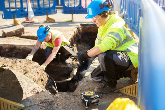 Two workers in hard hats and hi viz clothing working on underground cables