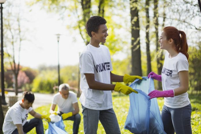 Environmental volunteering. Positive two volunteers holding garbage bag and looking at each other, representing public sector social value