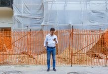 First official figures show BSR backlog rises to 36 weeks A young Caucasian man is standing in front of a construction site, using his phone and holding a file folder, representing the BSR backlog