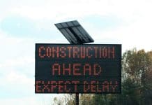 Strict deadlines and supply audits could help Britain’s infrastructure delivery backlog Portable solar powered highway sign indicating construction ahead expect delay, representing the UK's infrastructure delivery backlog