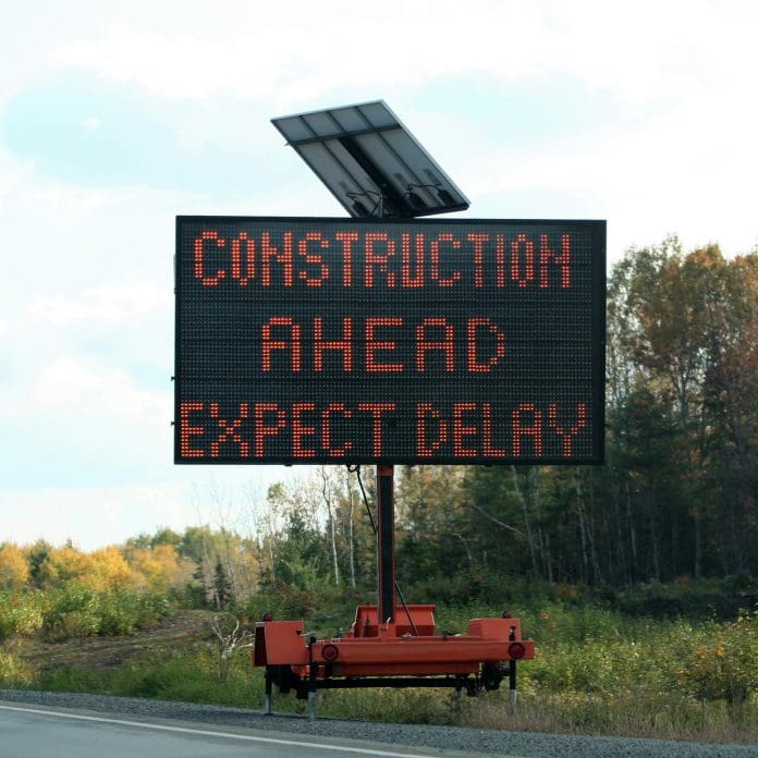 Portable solar powered highway sign indicating construction ahead expect delay, representing the UK's infrastructure delivery backlog