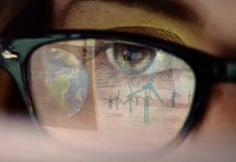 Why smart building management systems are now critical for sustainable urban growth Stock video close up clip of a young woman’s eye as she watches a large computer display, the reflection of the screen consists of the planet Earth & CAD design for a wind farm, representing Smart building management systems