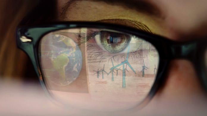 Working eye climate energy Stock video close up clip of a young woman’s eye as she watches a large computer display, the reflection of the screen consists of the planet Earth & CAD design for a wind farm, representing Smart building management systems