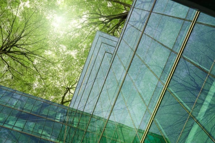 Eco-friendly building in modern city. Sustainable glass office building with trees for reducing carbon dioxide. Office building with green environment. Corporate building reduce CO2. Net zero emission