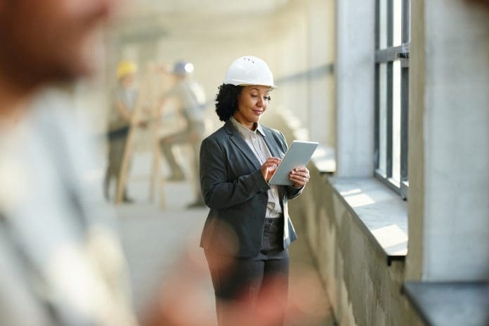 Smiling female building contractor working on touchpad at rebuilding site, representing construction ERP platforms