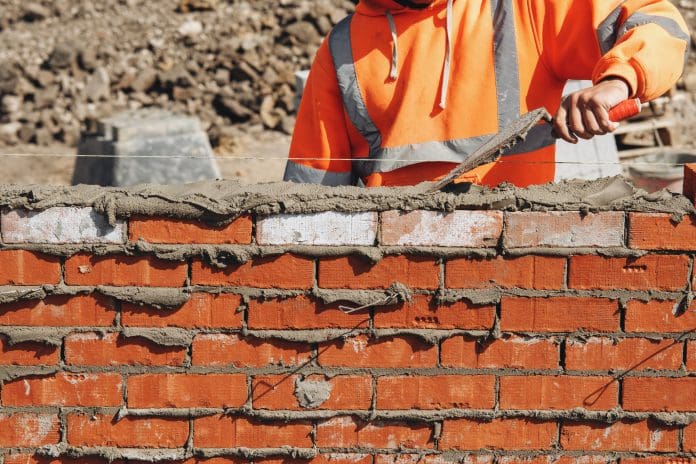Close-up of skilled bricklayer working on construction site laying bricks for wall construction