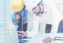 Industry leaders and government unite behind landmark Early Contractor Involvement research Close up of two architects or engineers discussing a project in a white office. They are wearing yellow and white hardhats and looking at a laptop screen. Toned image double exposure