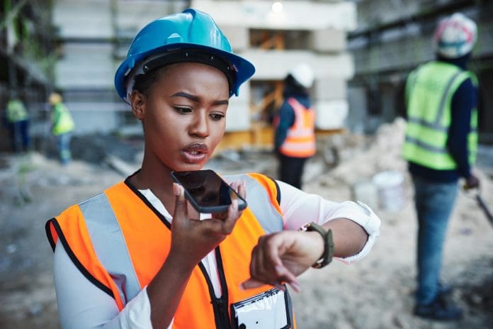 Shot of a young woman using a smartphone while working at a construction site, representing project delays caused by the building safety act