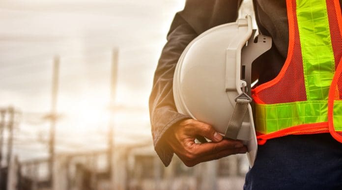 Technician holding white hat safety hard hat sunlight background, representing the need for preventative measures against Construction fatal injuries