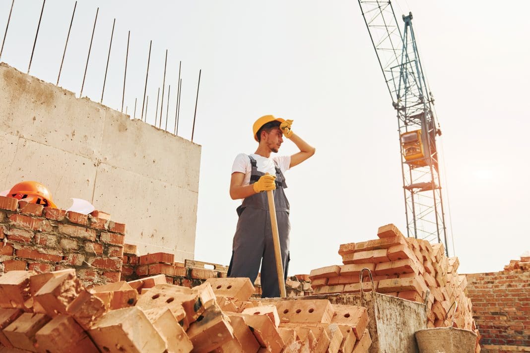 Tired man. Young construction worker in uniform is busy at the unfinished building The WHO and the WMO have published a new joint report and guidance on the growing global health challenges posed by extreme heat on workers