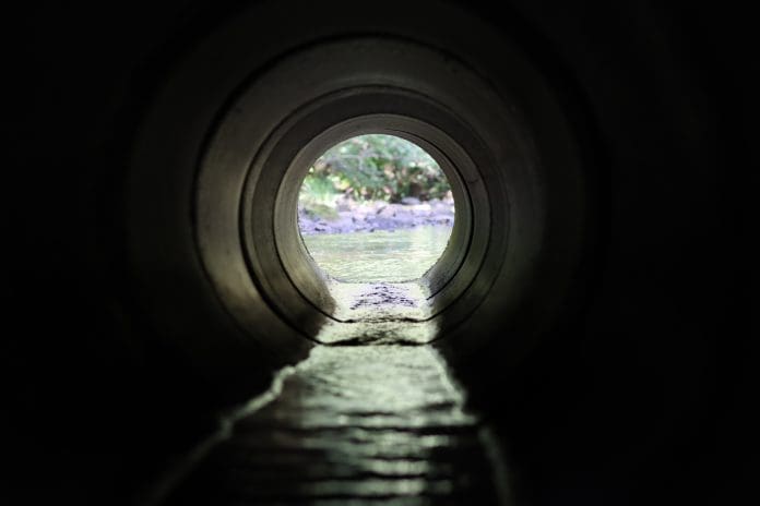 View through a round concrete tunnel carrying a water discharge beneath a road