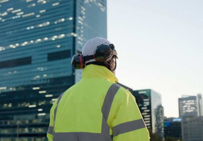 Man, construction worker and cityscape or office building development for civil engineering, planning or architect. Male person, hardhat and back in downtown New York for contractor, service or job