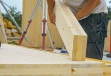 Mass timber is the perfect circular economy building material CLOSE UP, DOF: Unrecognizable male builder picks up a CLT beam from a workbench at an unfinished housing project. Contractor carries a glued laminated board across the bustling construction site, representing how Timber will be vital to construction circular economy, say Lamella