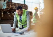 The role of information management tools in achieving project harmony Warehouse manager working on laptop while going through paperwork at lumber distribution department. Copy space.