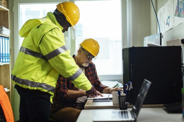 Two male engineers with the hardhats looking at the blueprints in their office at the construction site