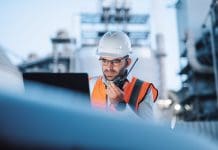 Why digital procurement platforms are powering construction’s digital leap in the age of AI A mid-adult male engineer works diligently during a night shift at an oil refinery, utilizing a laptop for monitoring operations and a walkie-talkie for real-time communication, representing digital procurement platforms