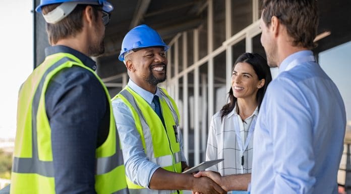 Smiling engineer shaking hands at construction site with happy architect. Handshake between cheerful african construction manager with businessman at bulding site. Team of workers with architects and contractor conclude an agreement with safety uniform, representing b2b marketing