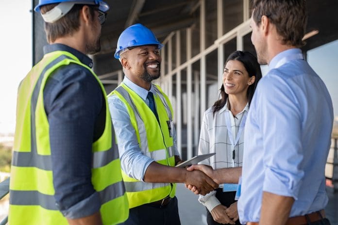 Engineer and businessman handshake at construction site Smiling engineer shaking hands at construction site with happy architect. Handshake between cheerful african construction manager with businessman at bulding site. Team of workers with architects and contractor conclude an agreement with safety uniform, representing b2b marketing