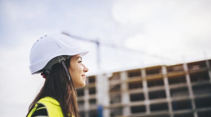 Side view portrait of beautiful woman architect standing in front on construction site at sunset.