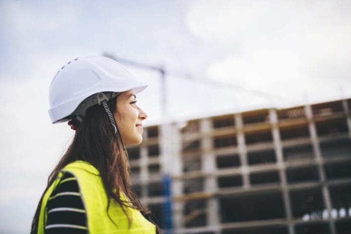 Portrait Of Woman Architect On Construction Site. Side view portrait of beautiful woman architect standing in front on construction site at sunset.