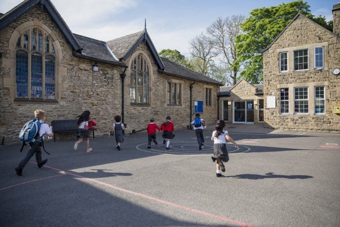 Time for School Rear view of children running in their school yard in the North East of England. They are all running towards the door with their backpacks on, representing reaching the 2028 RAAC removal deadline