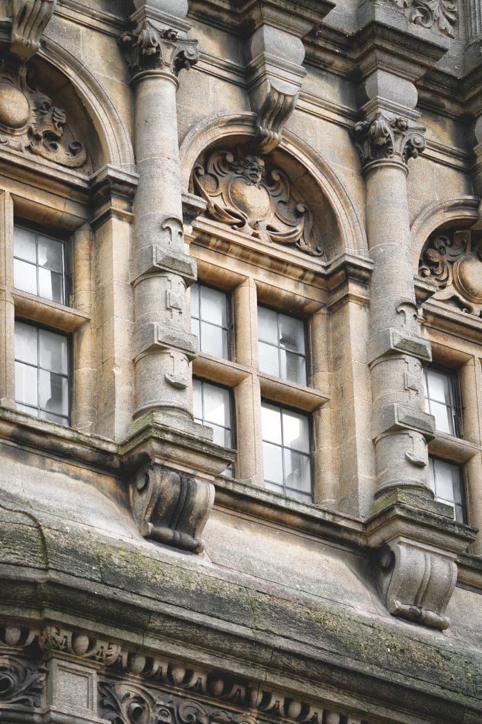Oxford historic Building Details, Architecture, Architectural Features, Oxfordshire, England, United Kingdom, Britain Oxford, UK – 20th March 2024: The building detail and architectural features of the building located at in Oxford, Oxfordshire, England, United Kingdom, Great Britain, Europe. No people seen in the photograph. Architectural Features of Central Oxford Building Location: Central Oxford, Oxfordshire, England, United Kingdom Date of Photograph: 20th March 2024 The building exhibits a blend of Gothic and Victorian architectural styles, common in central Oxford. The façade is characterised by ornate stone carvings and pointed arches. The structure primarily uses local limestone, which lends a distinctive warm, honey-coloured appearance, typical of many historic buildings in Oxford. Large, arched windows with intricate tracery and stained glass are prominent. The windows are set within deep reveals, providing a sense of depth and shadow. The roofline is punctuated by steeply pitched gables and decorative finials, contributing to the vertical emphasis typical of Gothic architecture. The main entrance features a grand, pointed arch doorway, often adorned with detailed stonework and flanked by columns. Elaborate cornices and parapets run along the building’s edges, incorporating decorative stone motifs such as fleur-de-lis and other heraldic symbols. The building maintains a balanced and symmetrical layout, with a clear emphasis on verticality and proportion. Flying and engaged buttresses are present, providing both structural support and decorative appeal. The architectural style reflects Oxford’s historical significance and its long-standing association with academia and ecclesiastical heritage. This building exemplifies the rich architectural tapestry of central Oxford, seamlessly integrating historical elements with a timeless aesthetic.
