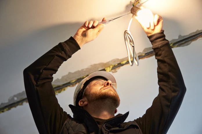 Portrait of male electrician, focused on wiring a temporary light bulb fixture on the ceiling, representing short training courses in electrical skills