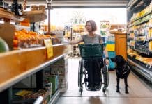 Everyday scenarios highlight the range of obstacles facing disabled people Woman on wheelchair and her service dog go shopping at local grocery store, representing some of the obstacles faced by disabled people