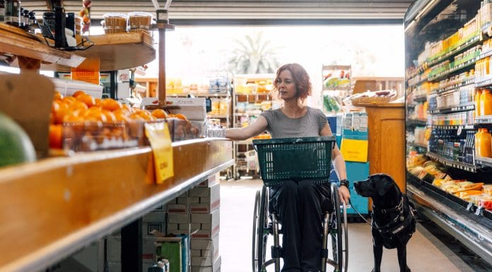 Woman on wheelchair and her service dog go shopping at local grocery store, representing some of the obstacles faced by disabled people