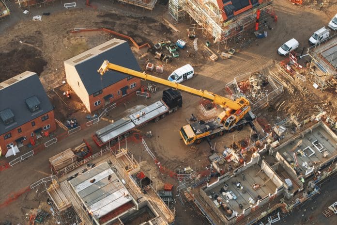 Aerial view of yellow mobile crane at construction site performing lifting operation, representing planning and infrastructure bill amendments
